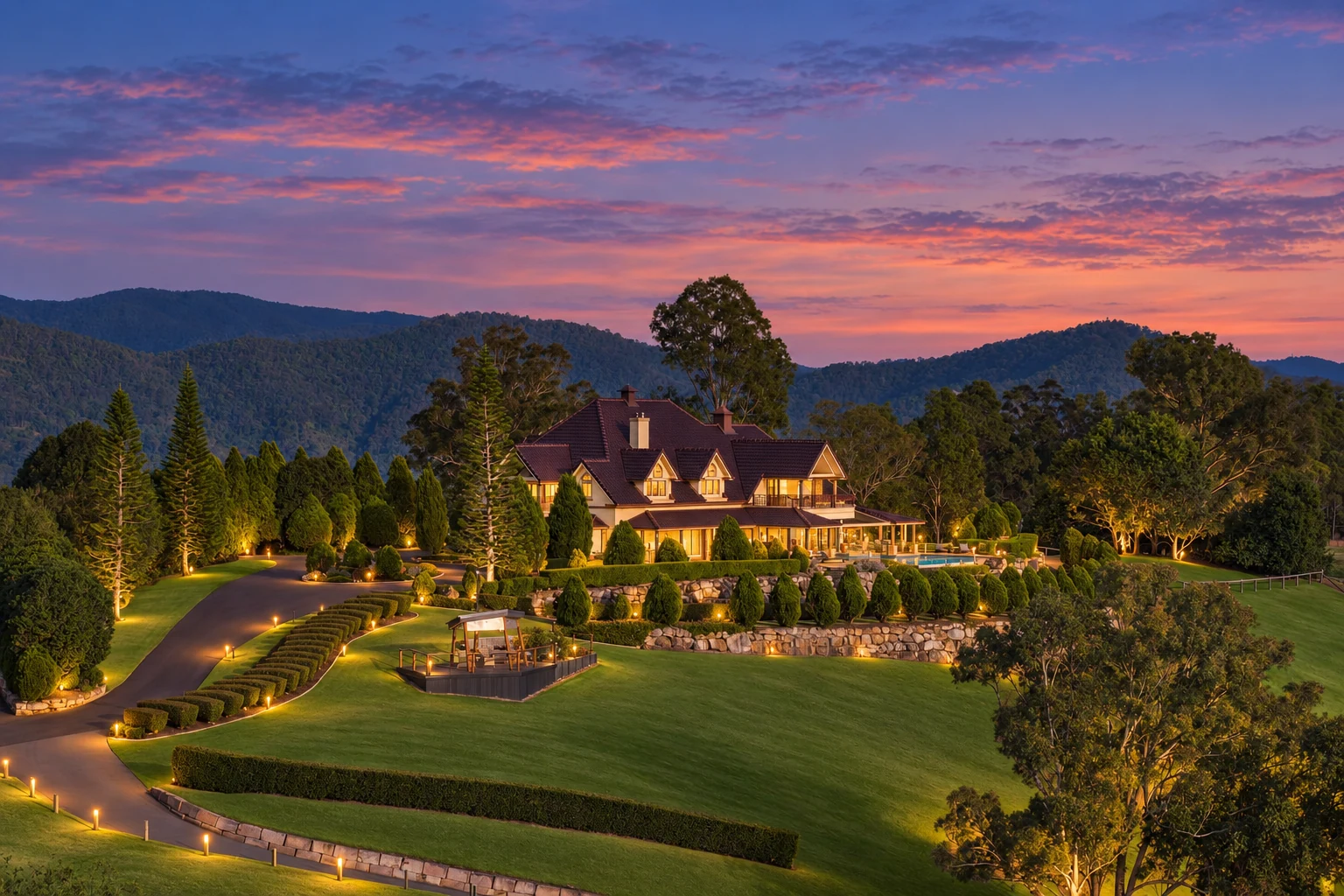 A homestead on a lit, terraced hilltop at dusk, looking out over forested ranges