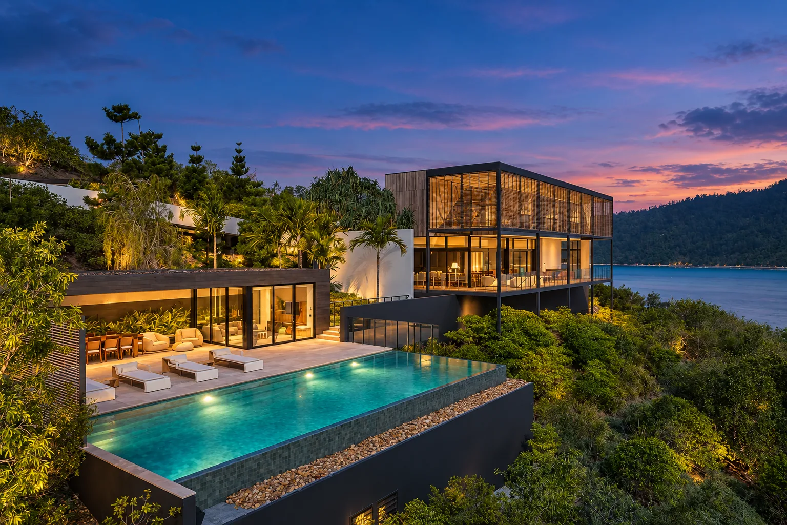 A low timber and glass residence above an infinity pool, on a headland looking out over water at dusk